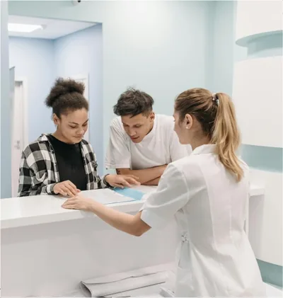 Two patients at a reception desk while a staff member helps them