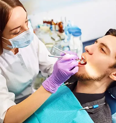 A clinician in purple gloves restores a tooth for a bearded man