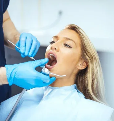 A woman lies back while gloved hands work with a mirror and scaler